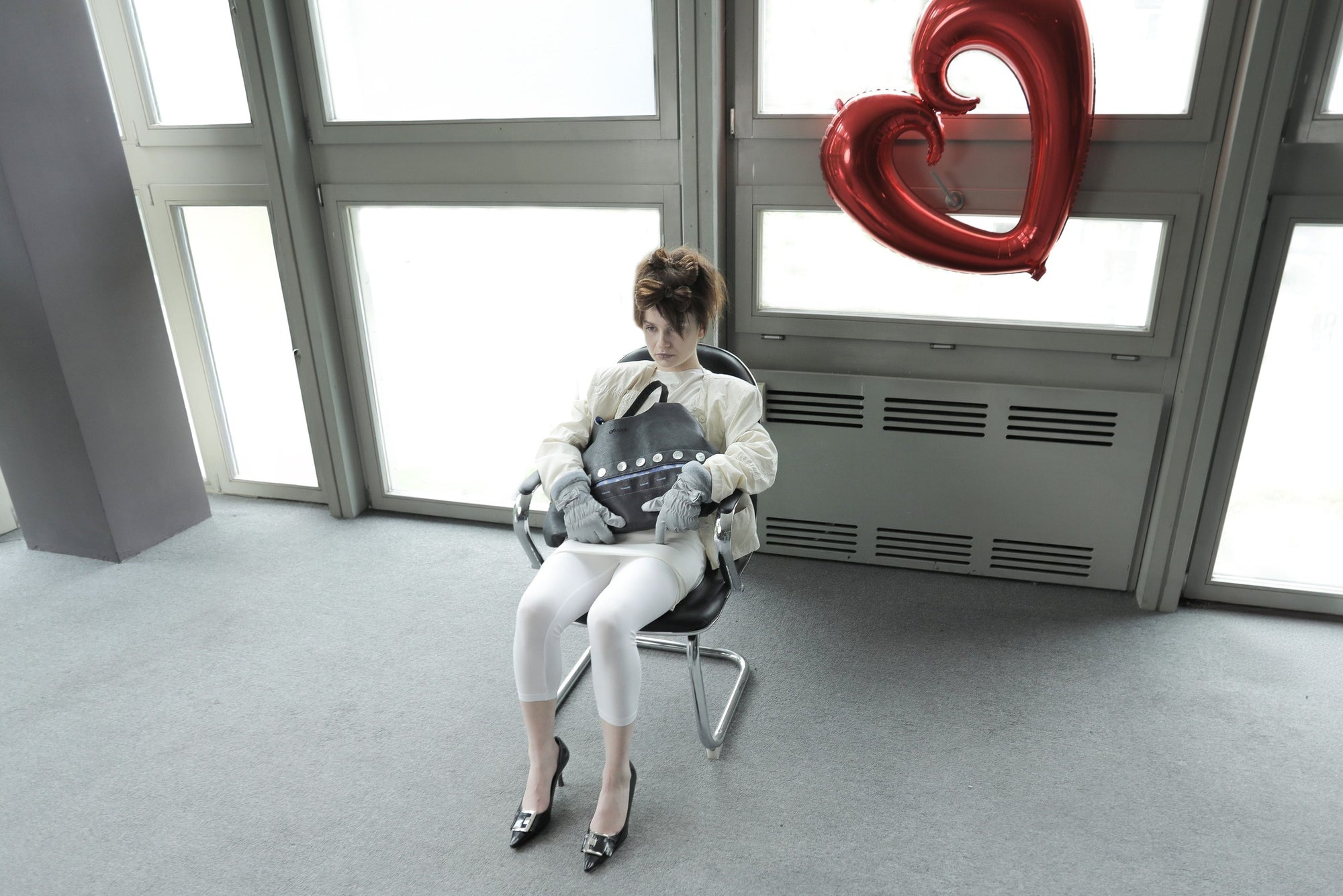 Model with edgy styling sitting in a chair, holding the Omashu Sylvie black shoulder bag, highlighting its button detail and slouchy form.