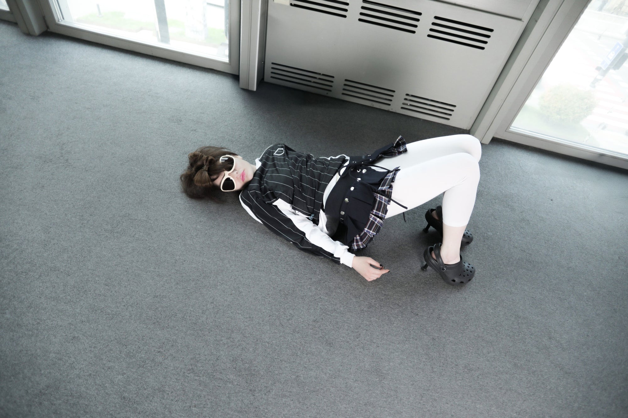Model wearing the Omashu AYA Belted Layered Skirt with a pinstripe top and white leggings, showcasing the skirt's dark top layer and plaid underlayer, viewed from above.