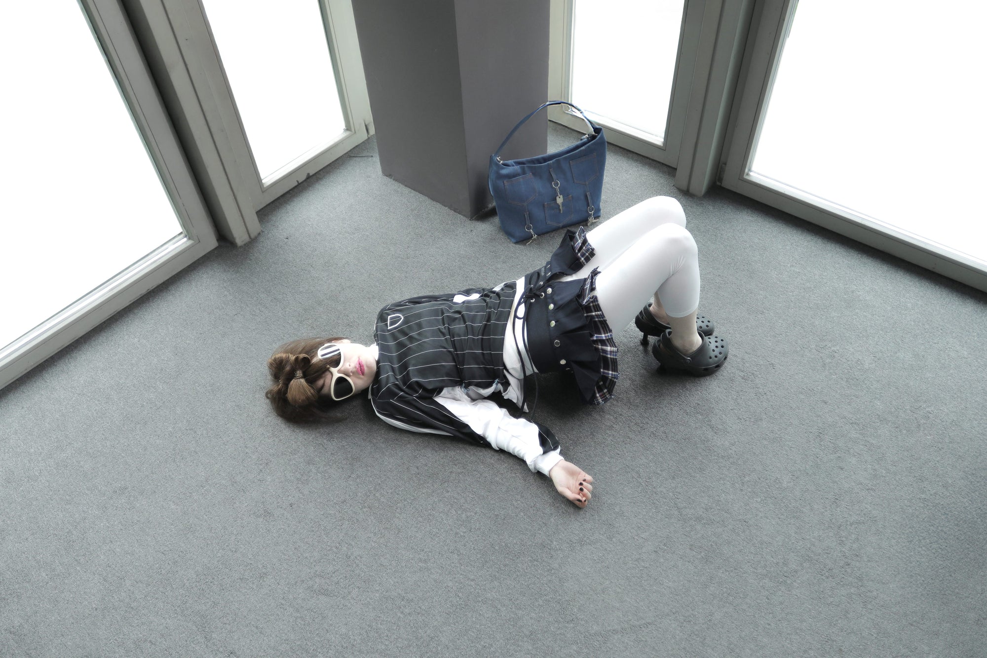 Overhead shot of a model on the floor styled in the Omashu AYA Belted Layered Skirt, featuring a dark solid top layer over a plaid pattern, with the Omashu Ines bag in the background.