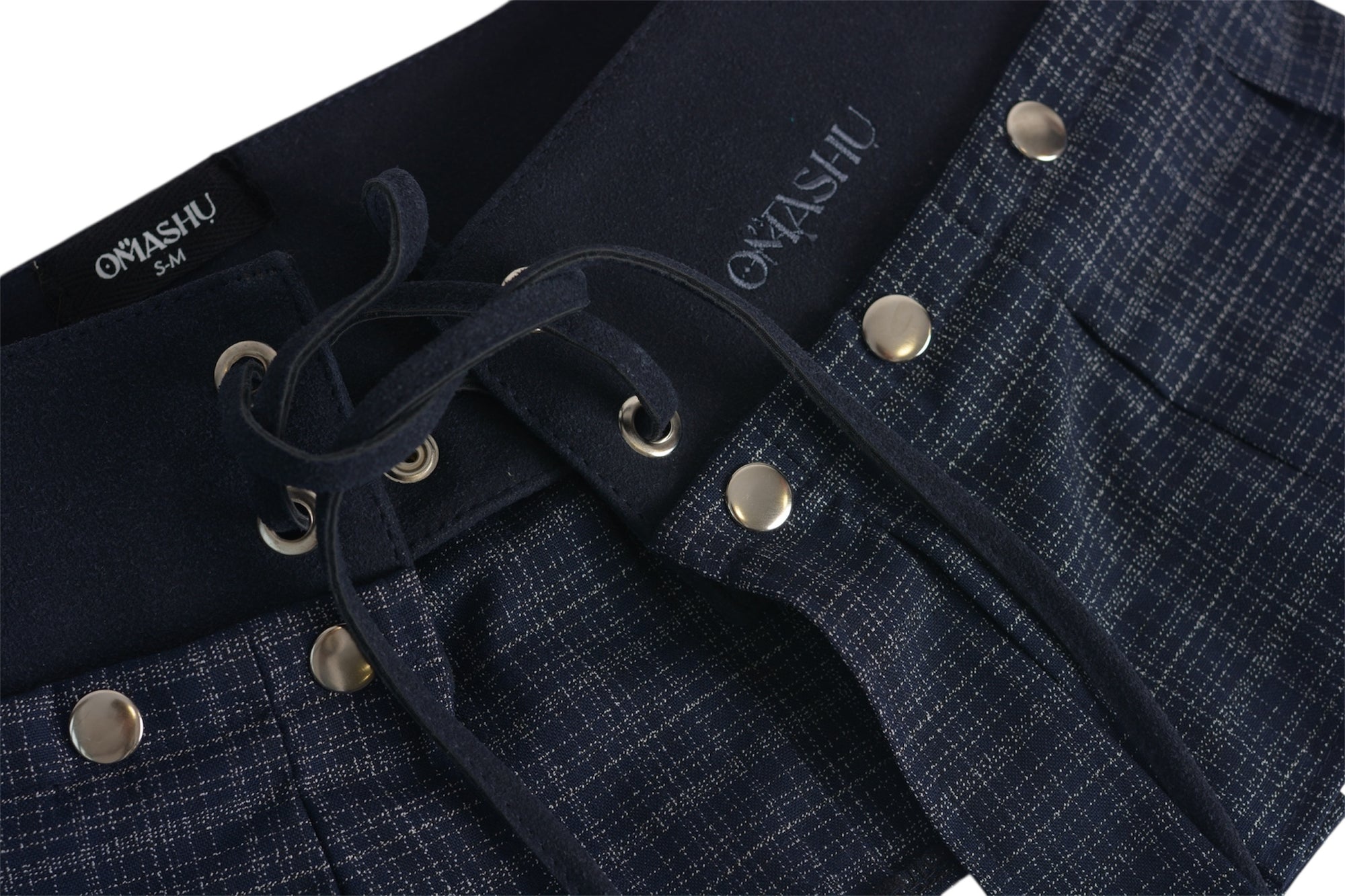 Close-up of the Omashu AYA skirt showing the texture of the pleated dark fabric, silver snap buttons, black lacing detail on the corset belt, and OMASHU brand tags.