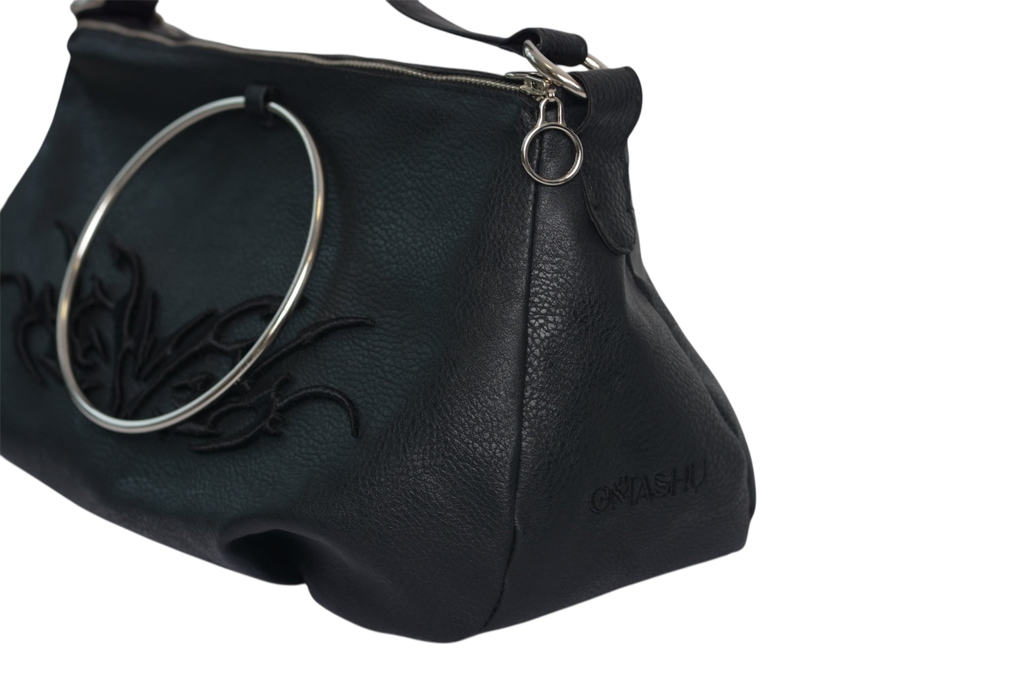 Close-up of Omashu Anya black faux leather bag showing silver-tone ring, tonal embroidered wing-like detail, and embossed Omashu logo on the side.