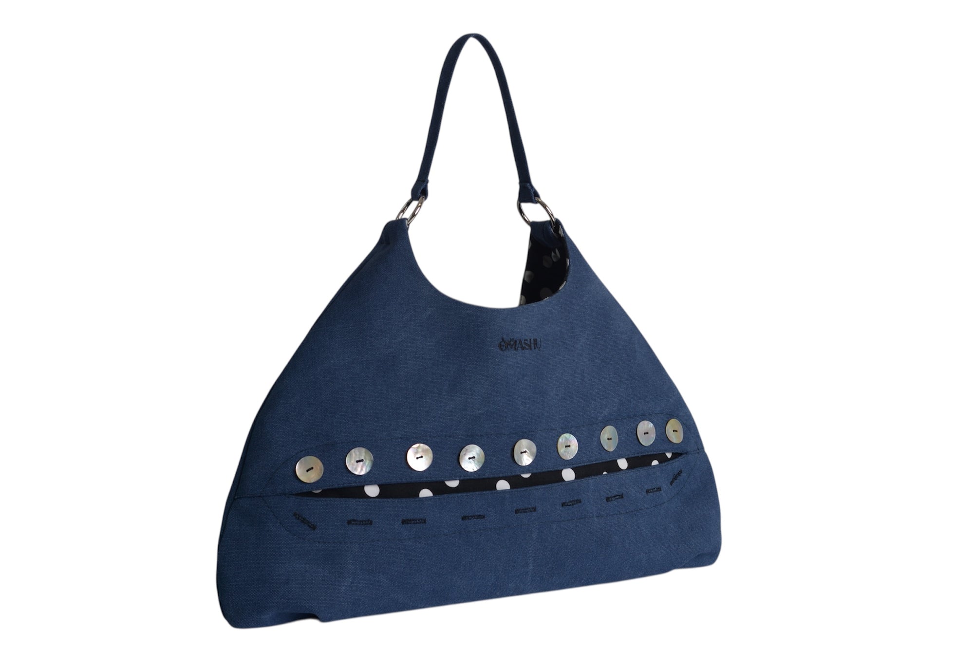 Omashu Sylvie Eclipse Bag in blue canvas-like material, featuring a row of mother-of-pearl style buttons revealing a black and white polka dot lining accent, angled front view.