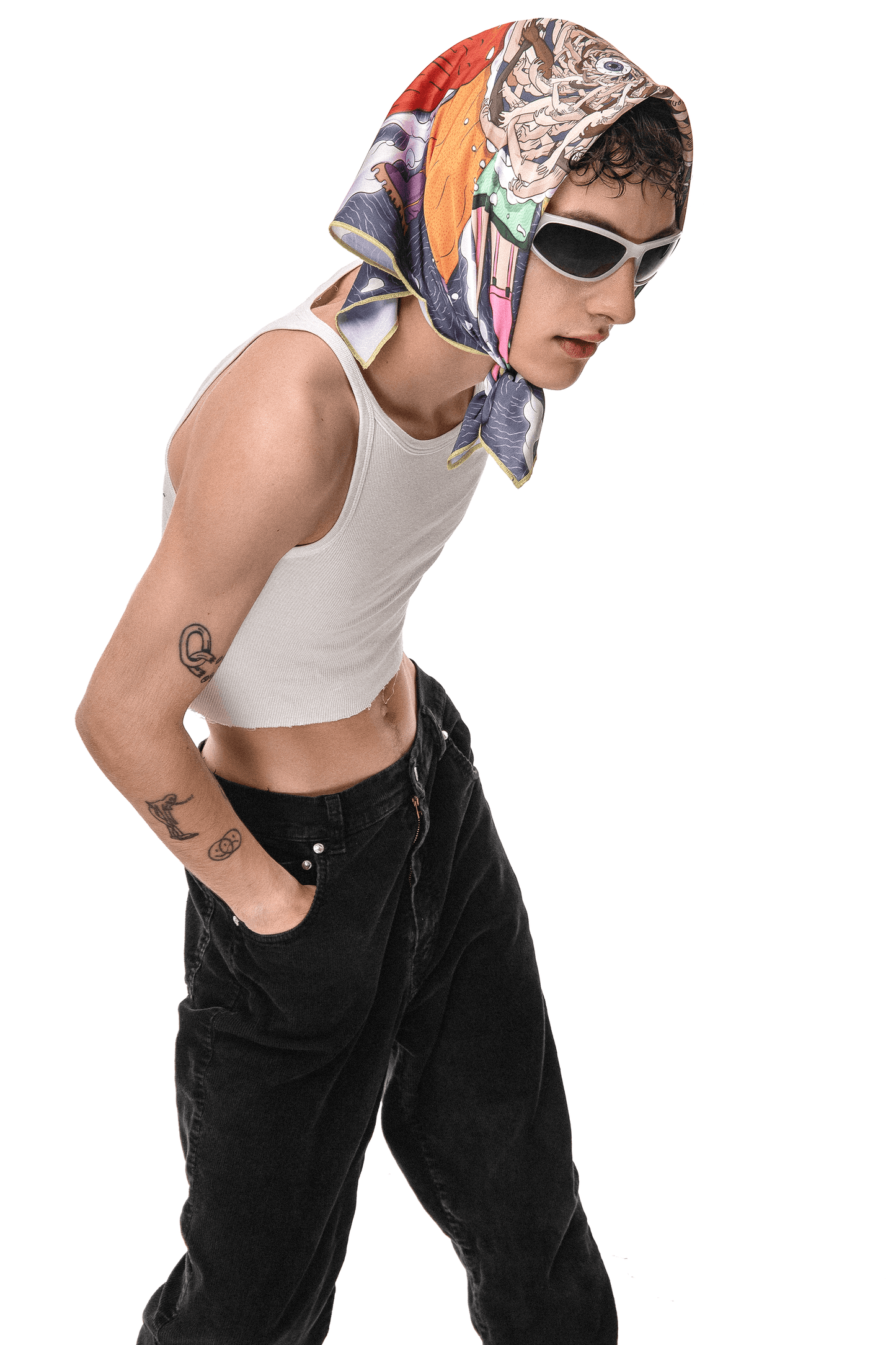 A person wearing a white tank top and black pants. The person is wearing a colorful scarf on their head with a pattern of flowers and leaves. The person has a tattoo of a snake on their left arm. The person is standing against a white background.