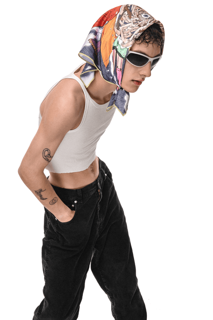 A person wearing a white tank top and black pants. The person is wearing a colorful scarf on their head with a pattern of flowers and leaves. The person has a tattoo of a snake on their left arm. The person is standing against a white background.