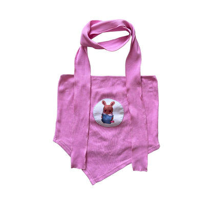 A pink tote bag featuring an embroidered patch of a cartoon-style bunny wearing a blue checkered outfit. The bunny is centered in a circular patch on the front of the bag. The bag has long pink handles, and the overall design is simple, with the bunny illustration as the focal point.