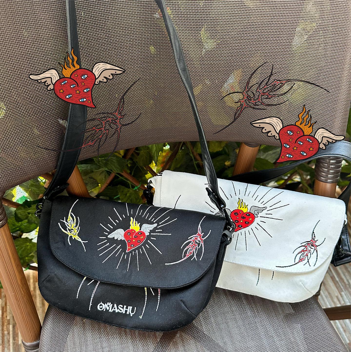 Two bags with unique designs on them. The bags are black, white, and black and white in color respectively. The designs on the bags are of red hearts with flames. The bags are resting on a wooden chair with a mesh background. The bags have a strap for carrying and a flap for closure. The bags have the text ‘OMASHU’ written on them.