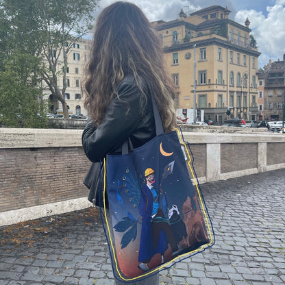 A photo of a person standing on a bridge in Rome, Italy, facing away from the camera and wearing a black leather jacket and carrying a large tote bag with a colorful illustration of a man in a blue suit and top hat, holding a cane and standing on a horse, against a background of a street with buildings and cars, and a yellow building with a green roof in the distance, with a cloudy sky and a gloomy mood.