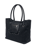 A black canvas tote bag with smooth black leather handles, a front zippered pocket, and silver-tone studs, shown on a light gray background.