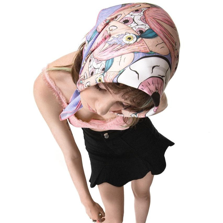 girl wearing OMASHU scarf on her head with the design exposed that containes huge eye. also she wears black skirt and pink top.