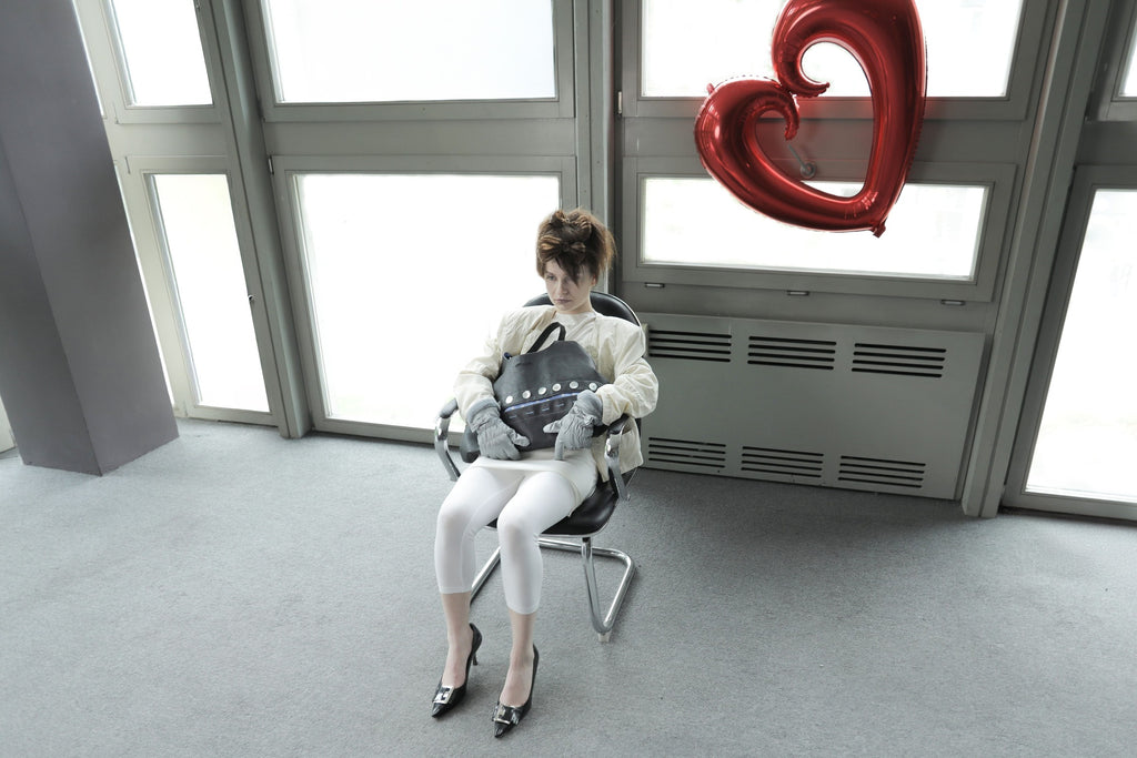 Model with edgy styling sitting in a chair, holding the Omashu Sylvie black shoulder bag, highlighting its button detail and slouchy form.