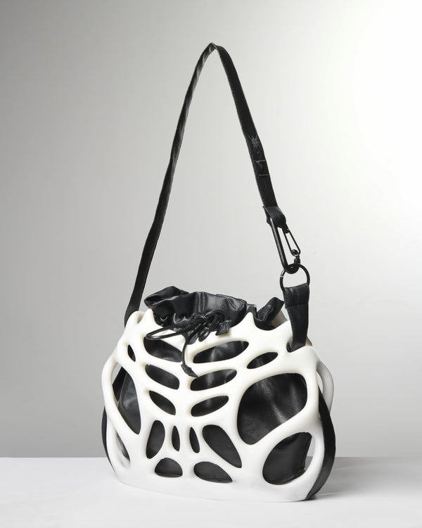 A white and black sculptural shoulder bag with an organic, open-frame structure and a black strap, photographed on a light gray studio background.