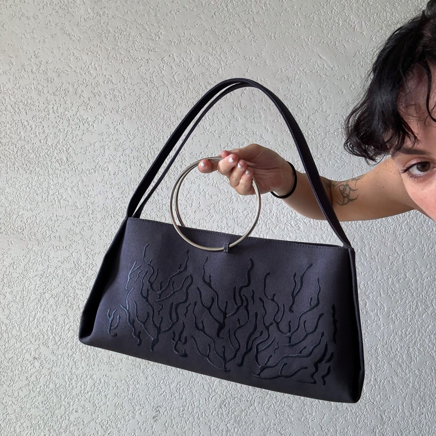 Gray handbag with a circular handle featuring an embossed or stitched flame-like design.