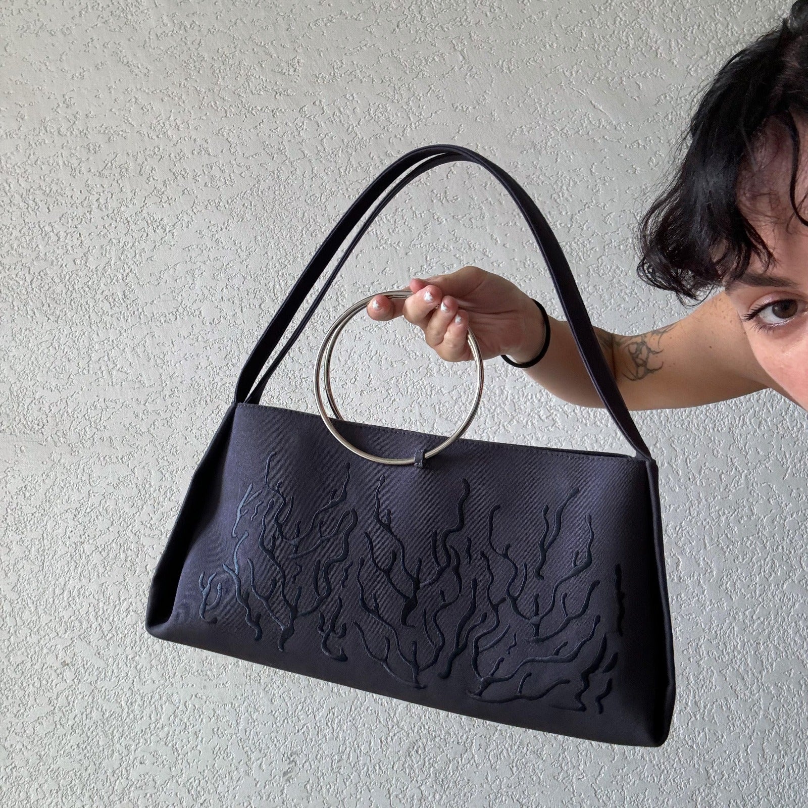 Gray handbag with a circular handle featuring an embossed or stitched flame-like design.