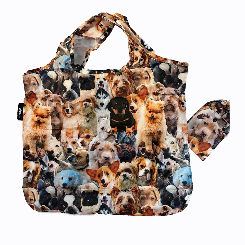 A fabric tote bag with a collage of various dog breeds such as golden retrievers, poodles, dalmatians, and bulldogs arranged in a grid-like pattern on a white background. The bag has a handle on top and features the brand name OMASHU.