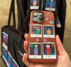 A close-up image of a brown smartphone case decorated with Polaroid-style patches featuring colorful cartoon animals from OMASHU. The case displays four characters: "Jiyah," "Mochi," "Dodo," and "Torti," each holding balloons or birthday-themed items. The background shows matching tote bags and hoodies with similar animal designs. The overall style is playful and whimsical, with bright colors and detailed illustrations of each animal character.