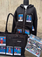 black merchandise from OMASHU featuring a hoodie and tote bag, both adorned with colorful Polaroid-style patches of animals. The hoodie displays multipale Polaroid patches of characters named "Mochi" and "Dodo," while the tote bag features additional characters like "Torti," "Toby," "Kittie," and "Jiyah." A display board featuring the same characters in a "dogs and cats edition" theme is also shown at the bottom right. The designs are vibrant and whimsical, with each animal wearing unique outfits and access