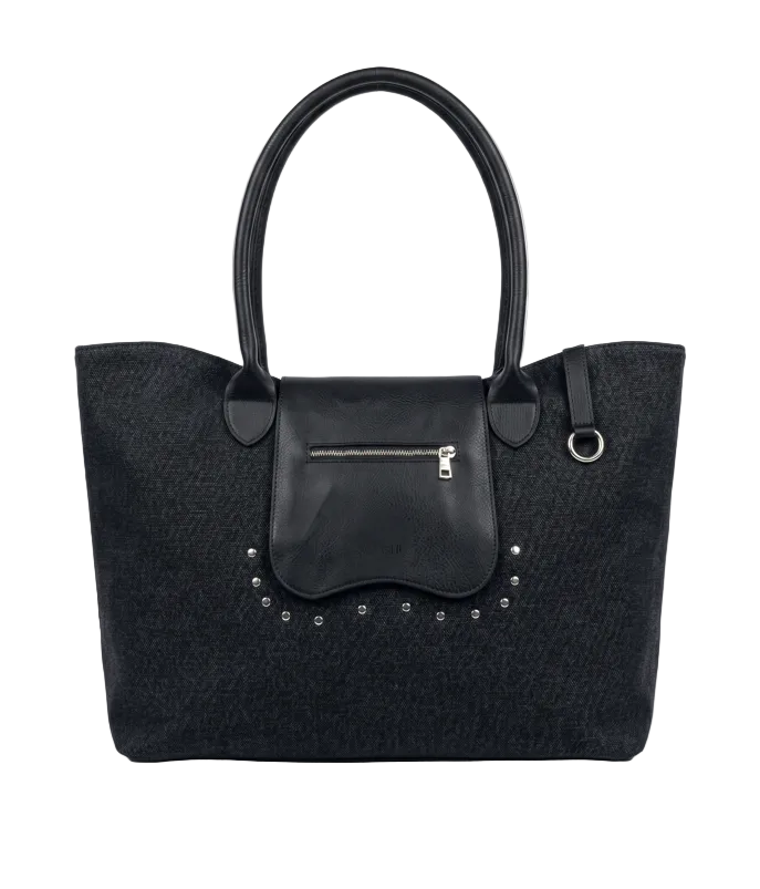 A black canvas tote bag with a smooth black leather front flap pocket, silver-tone zipper, and decorative silver studs, shown against a light gray background.