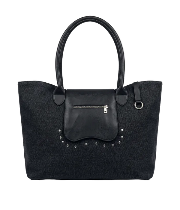 A black canvas tote bag with a smooth black leather front flap pocket, silver-tone zipper, and decorative silver studs, shown against a light gray background.