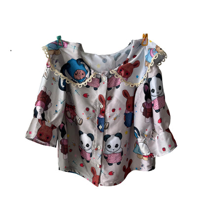 blouse with a playful design featuring various cartoon animals, including pandas, rabbits, and dolls in colorful outfits. The blouse has a white base with button closures, a lace-trimmed collar, and puffy sleeves, giving it a whimsical, youthful appearance. The animals are dressed in different cute patterns and colors, adding to the vibrant and fun aesthetic.