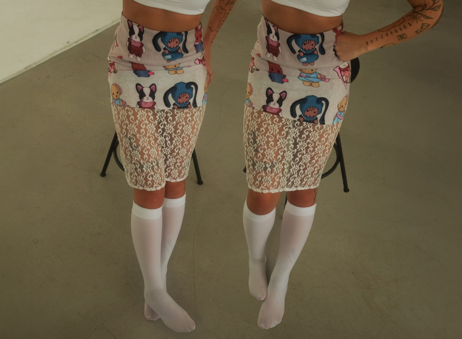 A person wearing a fitted skirt with the same cartoon animal pattern on top and a lace fabric below. The skirt is paired with white knee-high socks, and the image is mirrored to show the outfit from two angles.