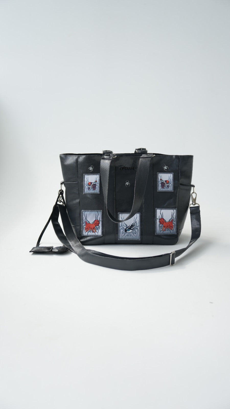 Omashu black tote bag with embroidered patches, laptop divider, and adjustable strap, showcasing bold streetwear accessory.