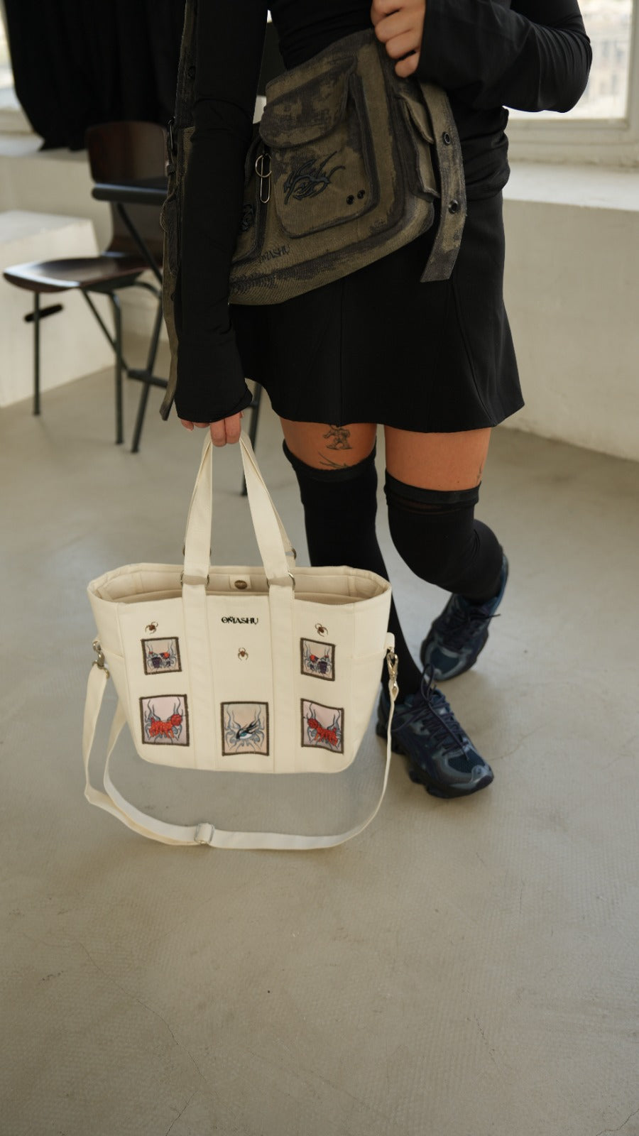 Model carrying Omashu white tote bag with embroidered patches, showcasing stylish streetwear accessory with laptop divider.