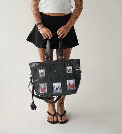 Model carrying Omashu black tote bag with unique embroidered patches, perfect for everyday use with laptop divider.