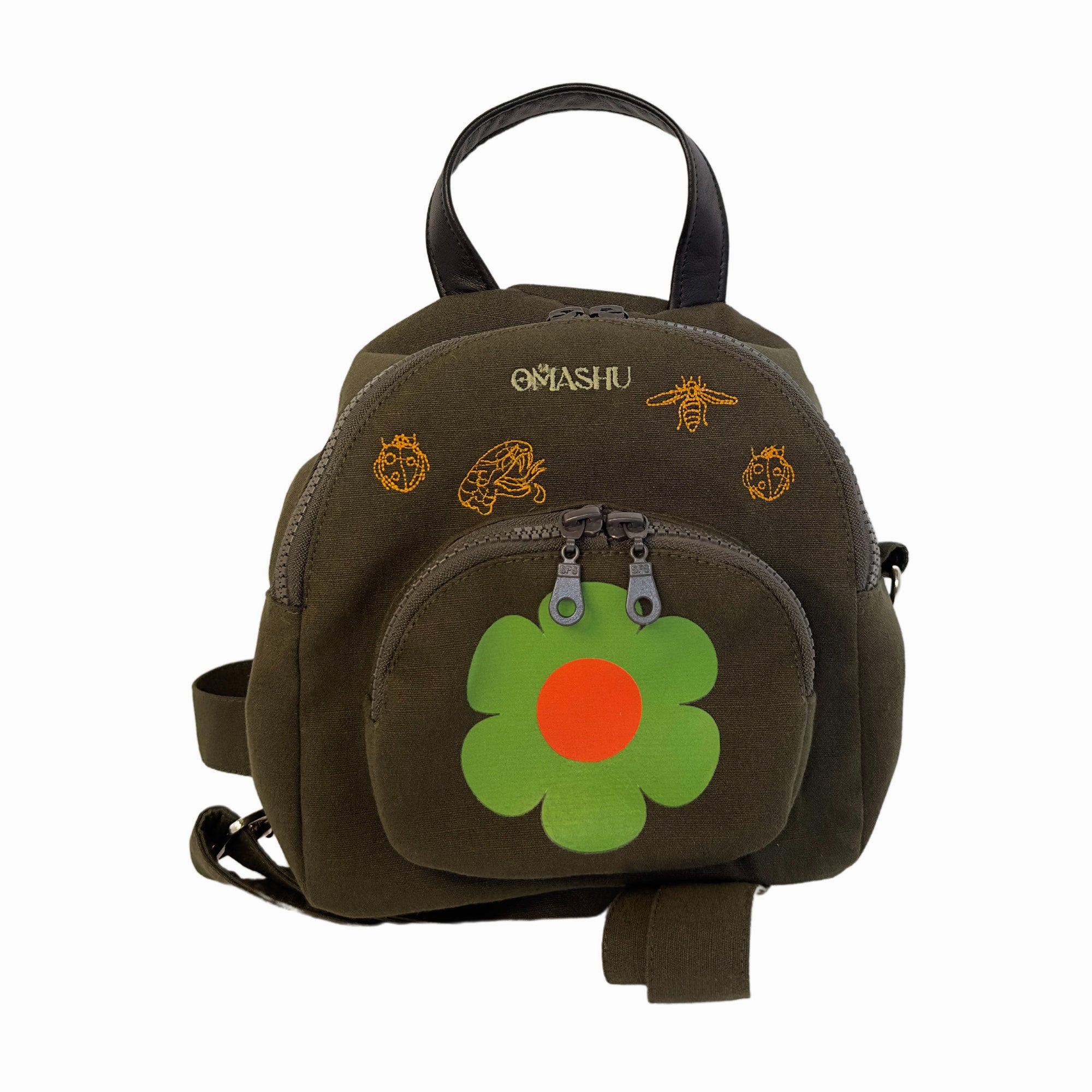 Small backpack with dark green fabric and lighter green flower design on front with small handle on top and two straps on back, zipper closure on top with two silver zippers, small logo on top left corner that reads ‘OMASHU’, and several small bee and flower designs scattered around front and sides.