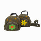 Two olive green backpacks with yellow and orange flower designs on them with black handle on top and black straps, zipper closure with green flower zipper pull, and the word ‘OMASHU’ written in yellow on top shown against white background.