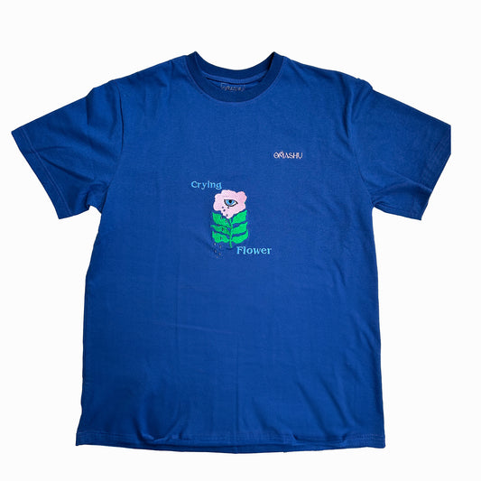 The graphic is of a pink and green flower with the word “Crying” above it and “Flower” below it. The t-shirt is a crew neck style with short sleeves. The t-shirt has a small logo on the right sleeve that reads “OMASHU”.