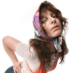 A photo of a person wearing a colorful headscarf with a pink and blue pattern, a white shirt, and an orange tank top, posing with their head tilted to the side and their hand on their hip, against a white background.