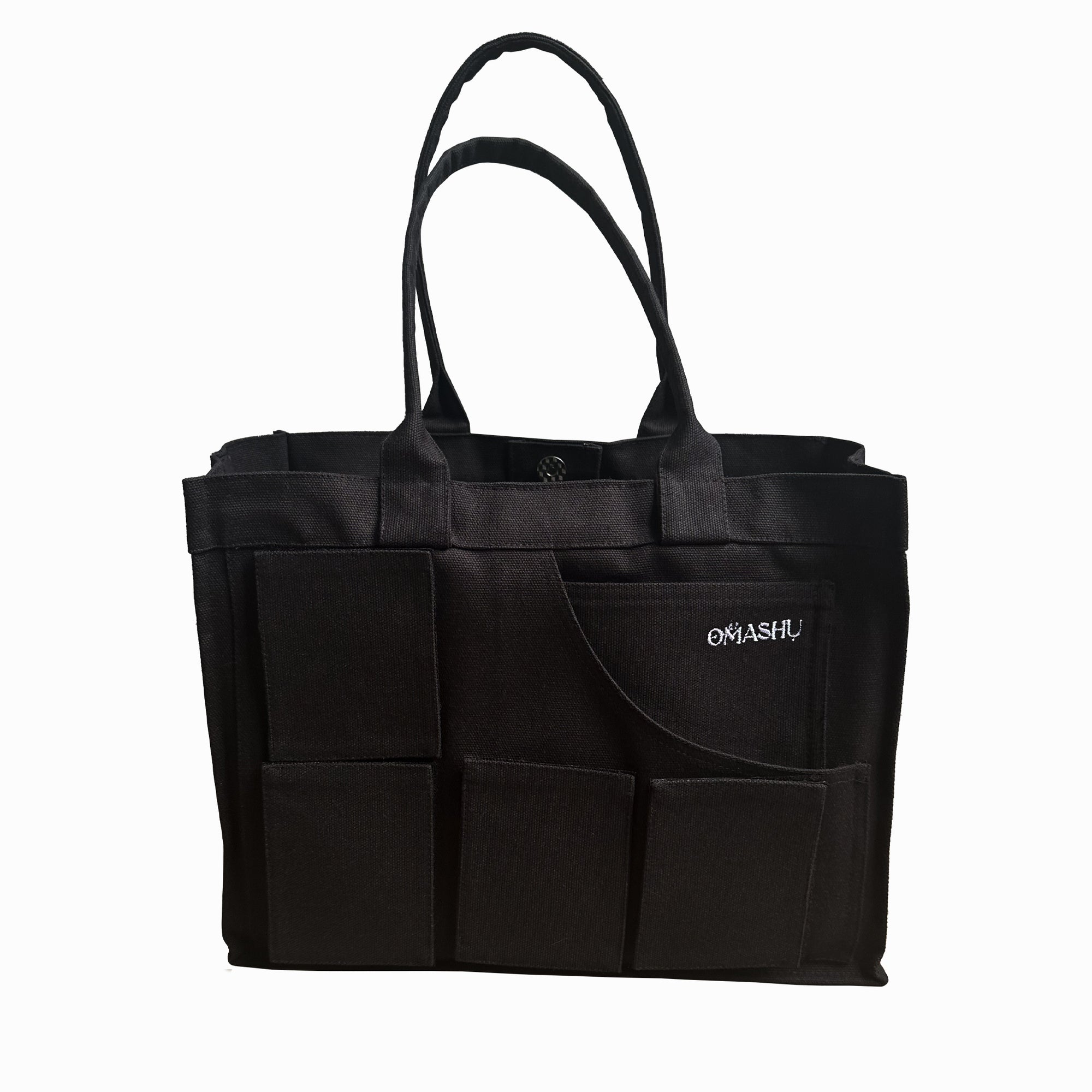 A black tote bag with multiple exterior pockets, featuring a simple design and sturdy handles. The brand name 'Omashu' is embroidered in white on one of the pockets.