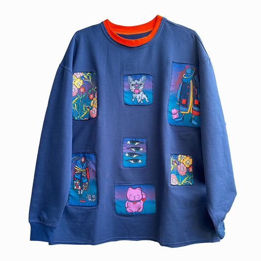 A blue long-sleeved t-shirt with colorful rectangular patches arranged in three rows of three patches each, featuring different designs including a cat, flowers, a robot, and flowers, with an orange collar, on a white background.