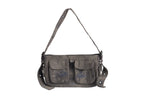 A dark gray canvas shoulder bag with a rugged, worn look, featuring two front pockets with flap closures and black embroidery designs on each pocket. The bag has an adjustable strap with metal eyelets and buckle details. A small black leather attachment hangs from one side of the bag, adding to its utilitarian aesthetic.