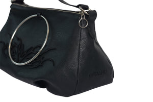 Close-up of Omashu Anya black faux leather bag showing silver-tone ring, tonal embroidered wing-like detail, and embossed Omashu logo on the side.