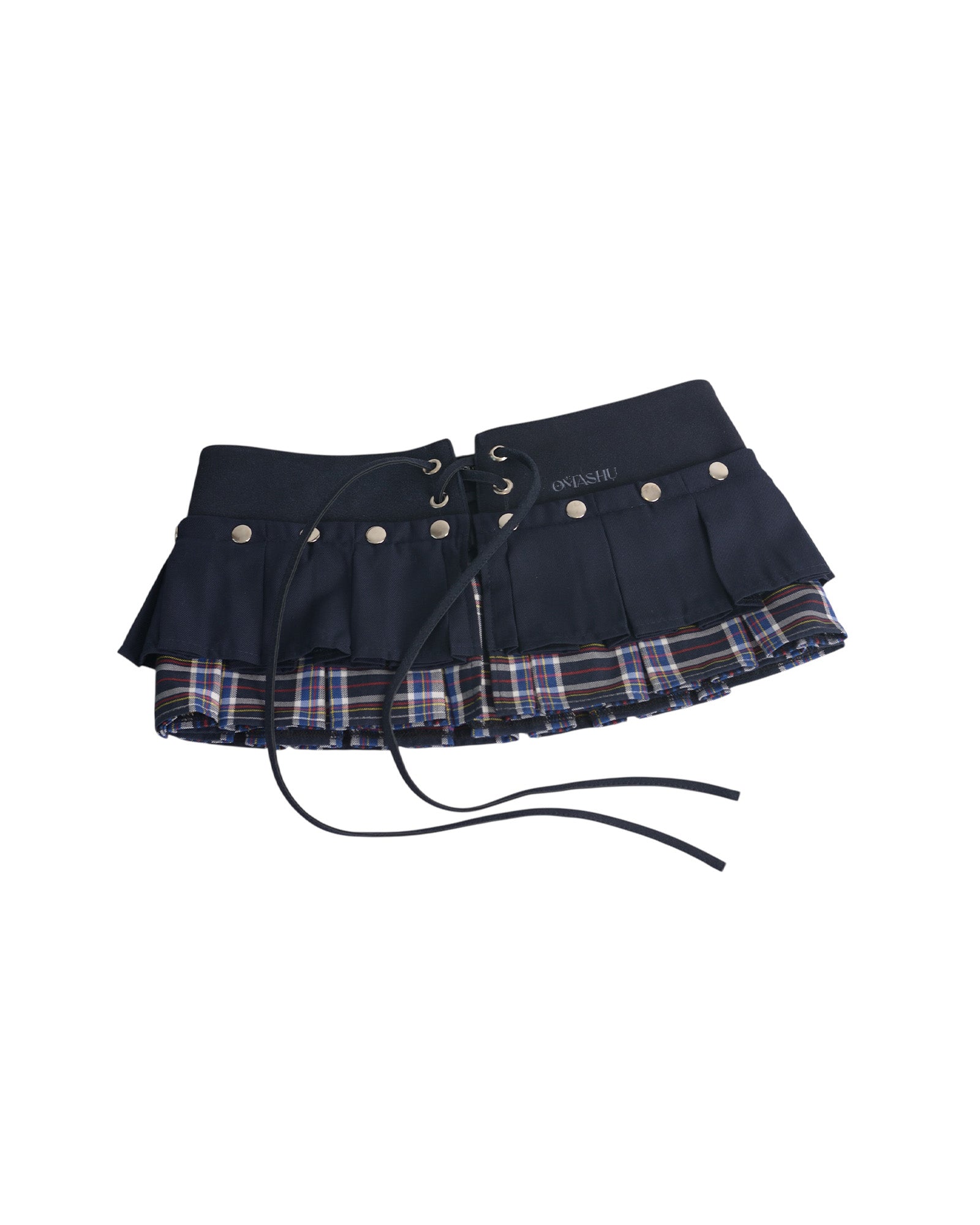 Omashu AYA Belted Layered Skirt, showing a dark navy pleated top mini skirt with silver snap buttons and an integrated corset belt with lacing, layered over a visible red, blue, and white plaid underskirt.