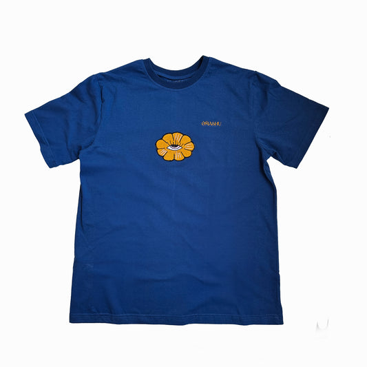 a t-shirt with flower design. The flower design is a simple line drawing of a orange flower with five petals and eye inside. The word “Omashu” is written in cursive above the flower design. The t-shirt is blue ,short-sleeved and has a crew neck.