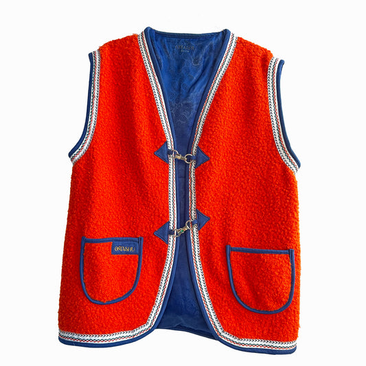 Red-orange vest with blue accents and white trim. The vest has a blue lining and two blue pockets on the front. It is closed with three silver clasps. The label on the left pocket reads ‘OMASHU’.