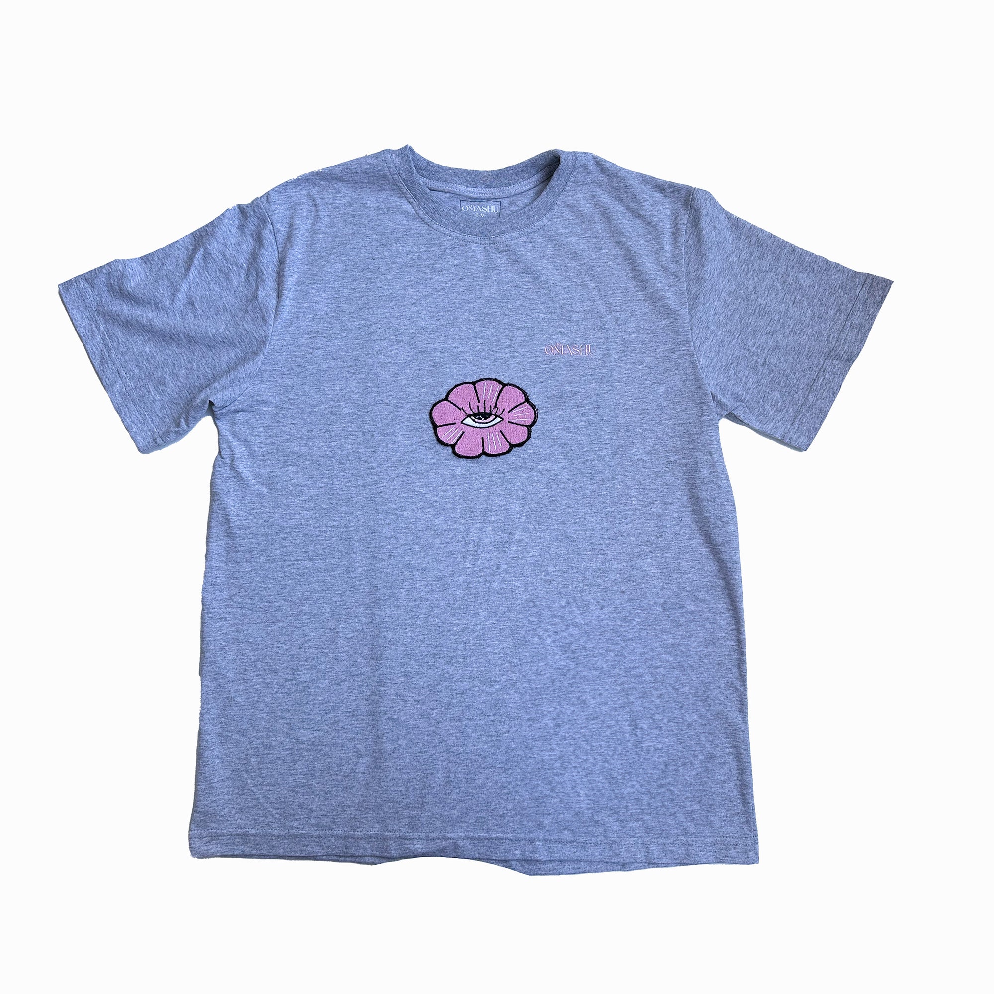 a t-shirt with flower design. The flower design is a simple line drawing of a pink flower with five petals and eye inside. The word “Omashu” is written in cursive above the flower design. The t-shirt is gray ,short-sleeved and has a crew neck.