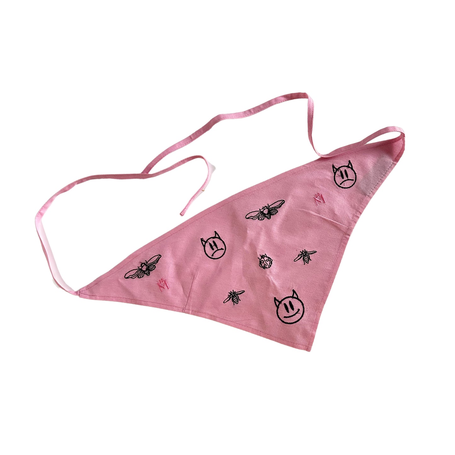 A pink scarf with black illustrations on it. The illustrations are of a cat face, a bee, a lightning bolt, and a spider. The scarf has two white straps for securing it to the face. The background is white.