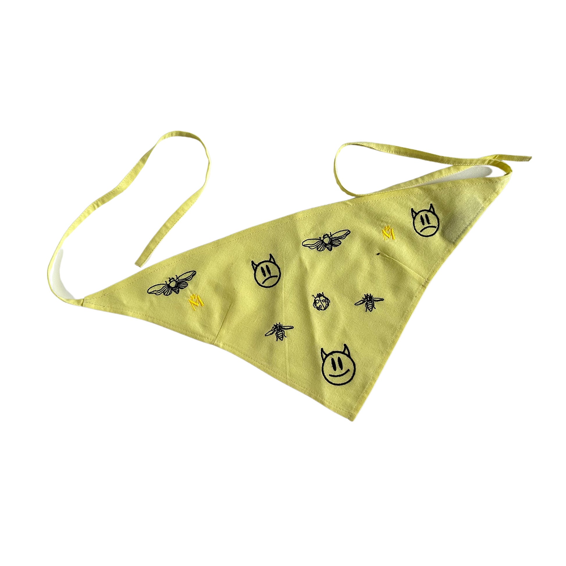 A yellow bandana with black designs on it. The bandana is triangular in shape with two strings attached to the top corners. The designs on the bandana are of bees, flowers, and cats. The background is white.