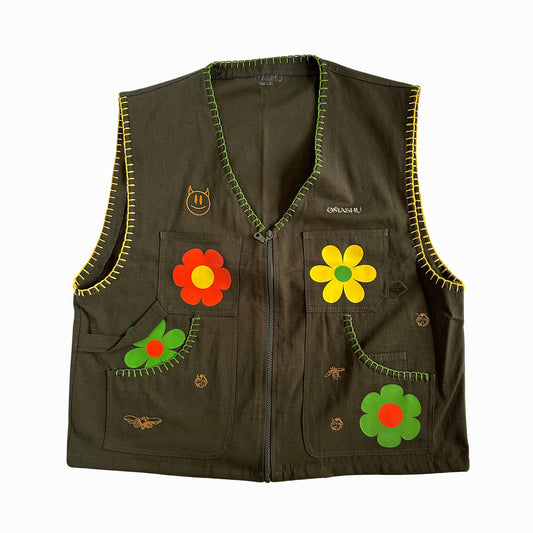 Green vest with yellow zigzag trim around edges and two large pockets on front with red, yellow, and green flower patches and small gold and silver embroidered details and small label on left pocket that reads ‘OMASHU’ displayed on white background.