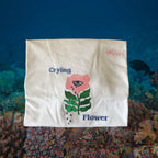folded white t-shirt with embroidered flower which has green stems and pink flower with eye in it. text says Crying Flower and brand is Omashu