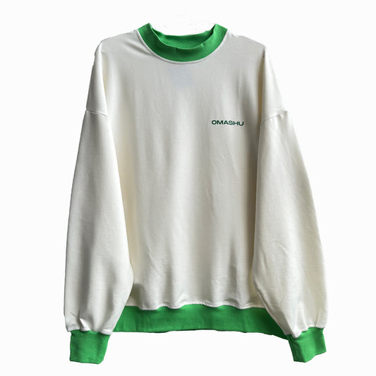 White and green sweatshirt with ‘OMASHU’ written in black letters on the chest. The sweatshirt has a loose fit and long sleeves. The green collar and cuffs add a pop of color to the white background.